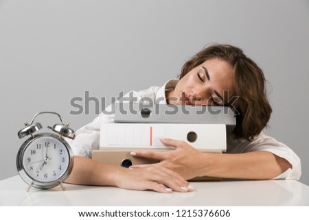 Image of young sleeping business woman isolated over grey wall background sitting at the table with folders.