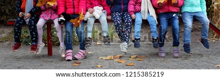 Group of diverse kids sitting together on the bench in the kindergarten, autumn outdoor, fashion and style Royalty-Free Stock Photo #1215385219