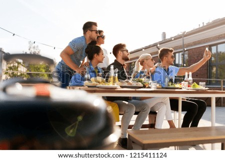 leisure and people concept - happy friends with drinks having barbecue party on rooftop in summer and taking selfie by smartphone