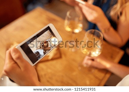 people, technology and lifestyle concept - hand of woman picturing food by smartphone and drinking wine at bar or restaurant