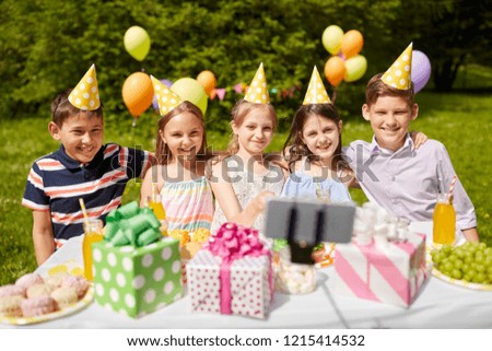 holidays, childhood and technology concept - happy kids taking picture by selfie stick on birthday party at summer garden