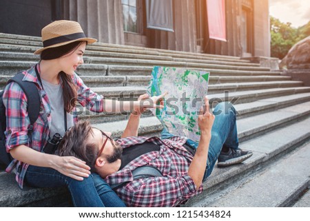 Nice picture of young tourists on stairs. She sits there and points on map. He holds map and lies on woman's knees.