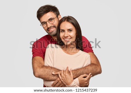 Lovely couple have warm cuddle, pose for family portrait, smile joyfully, have good relationships. Affectionate brother embraces his sister isolated over white wall. Girlfriend and boyfriend have date