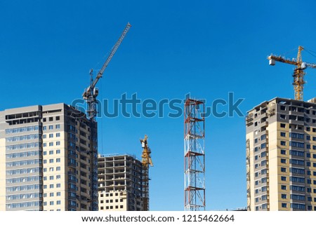 High-rise cranes and building under construction against blue sky. Construction of a modern residential complex.