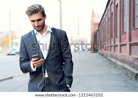 Happy attractive young businessman walking and using mobile phone outdoors