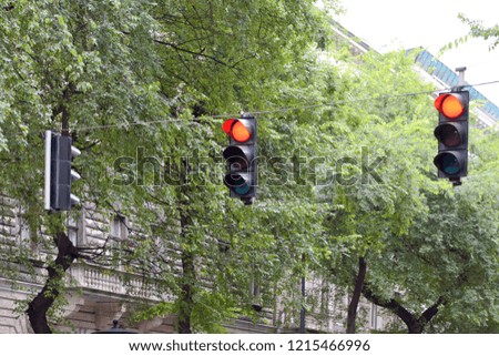Two red traffic lights with building and green trees on background