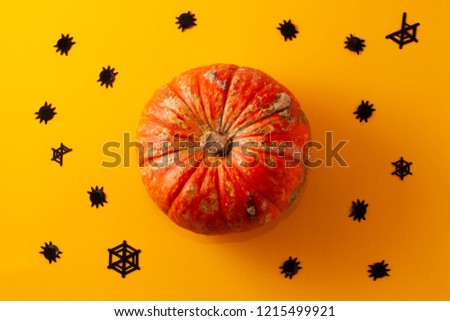 Conceptual halloween flat lay layout on a yellow-orange background. Hand-made confetti in the form of spiders and spider webs and decorative pumpkin.