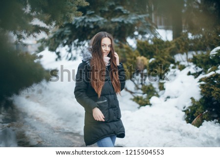 Beautiful brunette with long hair in a black jacket walks in the winter city