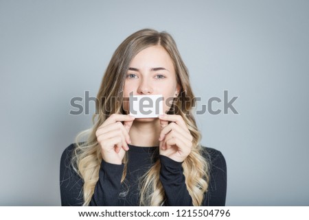 beautiful blonde woman holding a sticker in mouth, isolated over a gray background