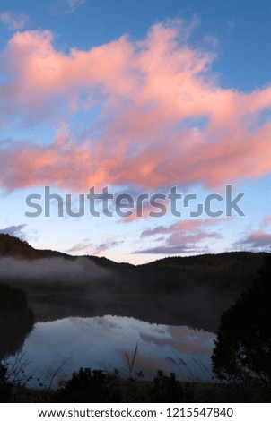 Blue sky, red clouds over the peaks of the mountains, the lake reflects the colors of the sky and clouds.