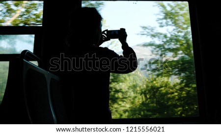 Silhouette of a girl takes pictures on the smartphone a mountain view of their train window, traveling by rail