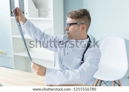Young caucasian doctor sitting in his office and looking X-ray image