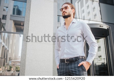Beautiful male model stands and poses. He looks stylish. Young man wears sunglasses and look forward. He is attractive and handsome.