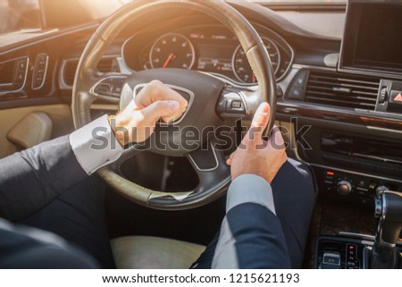 Picture of man's hands using warning on steering wheel. He drives. It is sunny outside.