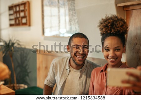 Young couple smiling and taking a selfie together while sitting at a table in a trendy bar