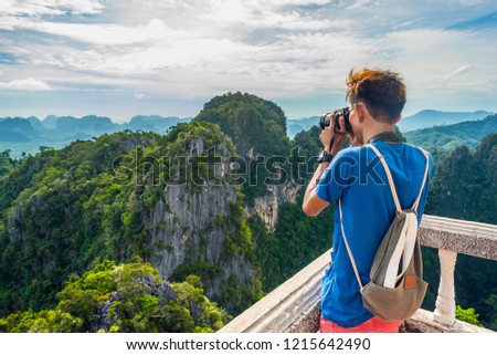 Young Thai traveler takes a photo of mountains covered with the jungle from the Tiger Cave Mountain Temple in Krabi, Thailand.