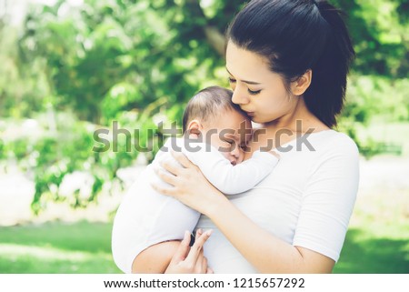 Beautiful attractive asian mum holding and hug her newborn baby ,kissing baby  sleeping in park on morning sunshine day.