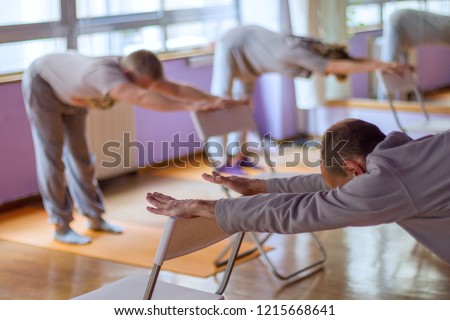 Yoga class, downward facing dog with the help of a chair done by three practitioners. Royalty-Free Stock Photo #1215668641