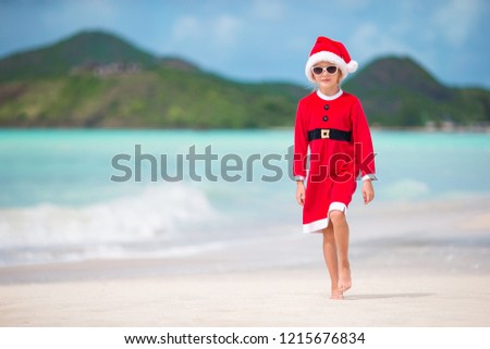 Adorable little girl in Santa hat and costume on tropical beach