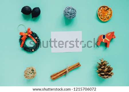 Creative flat lay of christmas ornaments in minimal style with blank greeting card on green background, holiday concept