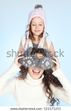 Happy mother and smiling little daughter in winter clothing over blue