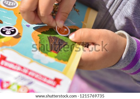 Child plays a pirate quest on a paper map, hands glue a sticker Royalty-Free Stock Photo #1215769735