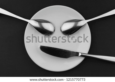 Conceptual face of a ceramic board two metal spoons and a knife
