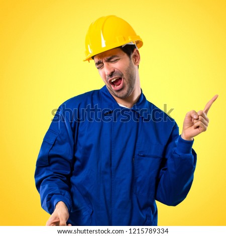 Young workman with helmet enjoy dancing while listening to music at a party on yellow background