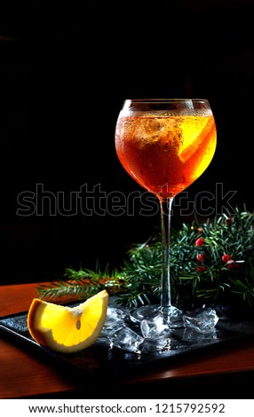 Vertical view Aperol Spritz cocktail in frozen glass with orange slices ice cubes with fir tree branches on black tray dark background for celebration Christmas New Year Holidays Party. Copy space