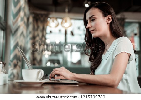 Profile picture. Pleased female person sitting at the table while typing message