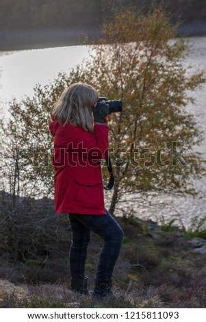 Side view, blonde, Caucasian female taking photographs near a reservoir. 