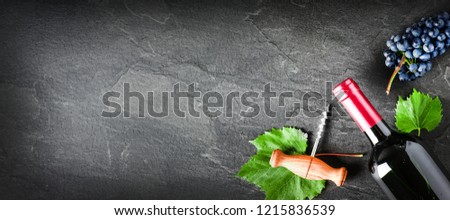 Bottle of red wine and fresh bunch grapes on dark stone table. Vine alcohol bottle on black background banner or copy space. 