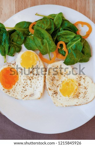 Fried eggs in the form of hearts with fresh spinach leaves and chopped orange bell pepper. On a white plate.Macro picture. Morning. Breakfast.
