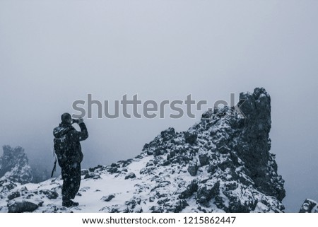 Traveler at the top of the mountain takes pictures of a lonely rock in the fog during a snowfall