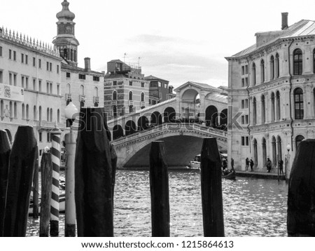 Black and white picture of Rialto bridge in canal Grande with  dock for boats.
