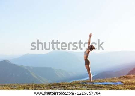 Female practicing sun salutation and doing morning yoga on top of a mountain in peaceful and quiet environment Royalty-Free Stock Photo #1215867904