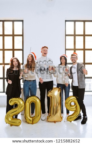 Group of young creative coworkers celebrating Happy New year 2019 in modern office. Happy people holding inflatable golden numbers with sparkling bengal lights celebrating and having fun.  Christmas.