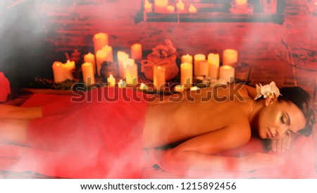 Massage Filipino of woman in spa salon. Girl on candles aglow background in steam room. Luxary ayurveda interior in oriental therapy salon. Photo effect with red toning. Artistic effect of steam