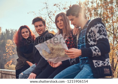 Photo of young friends looking at map and planning trip at autumn forest.