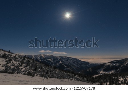 the moon shines on the snowy landscape of the mountains and clouds fly on the horizon