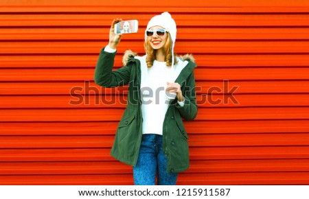 Fashion happy smiling woman taking selfie by smartphone on red background
