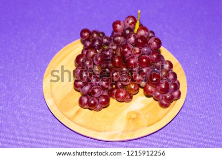 Grapes on brown wood plate in purple background. Select focus.