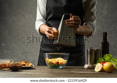 Chef throwing cheese into a bowl of Greek salad and seafood, cooking, restaurant concept, against a concrete wall with space for text