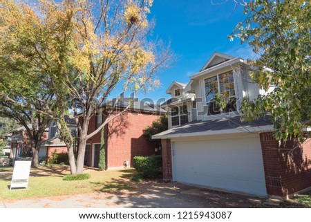 Home in suburban Dallas-Fort Worth with empty house for sale by owner yard sign. Colorful autumn fall foliage in Texas, North America.