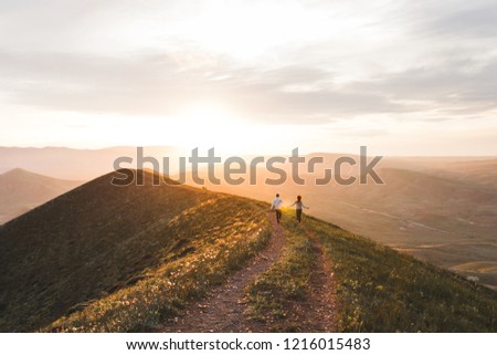 Young couple running together by sunset hill with amazing mountain view