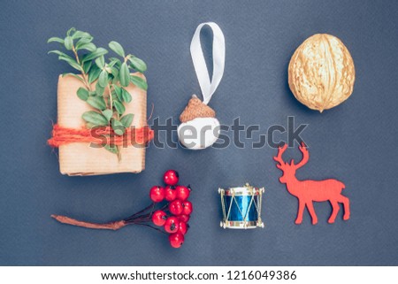 Christmas gift-box, nut, berry, a stencil of deer, decorative acorn and drum on the dark blue background.