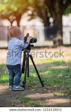 Two years old boy is photographer. Little boy photographing on the camera on tripod in the park.