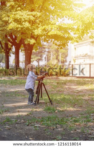 Two years old boy is photographer. Little boy photographing on the camera on tripod in the park.