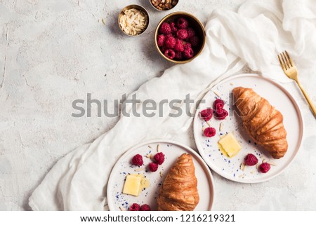Croissants with butter and raspberries on ceramic modern plates and light background