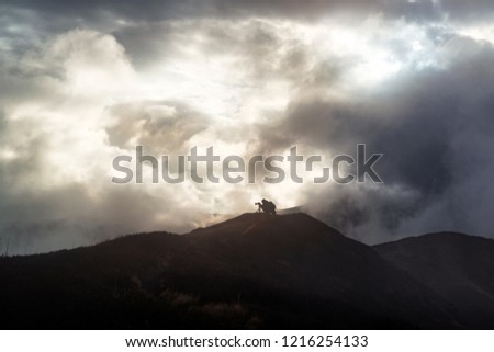 Photographer takes pictures on the top of a mountain with dramatic rainy clouds around. Challenging weather conditions
